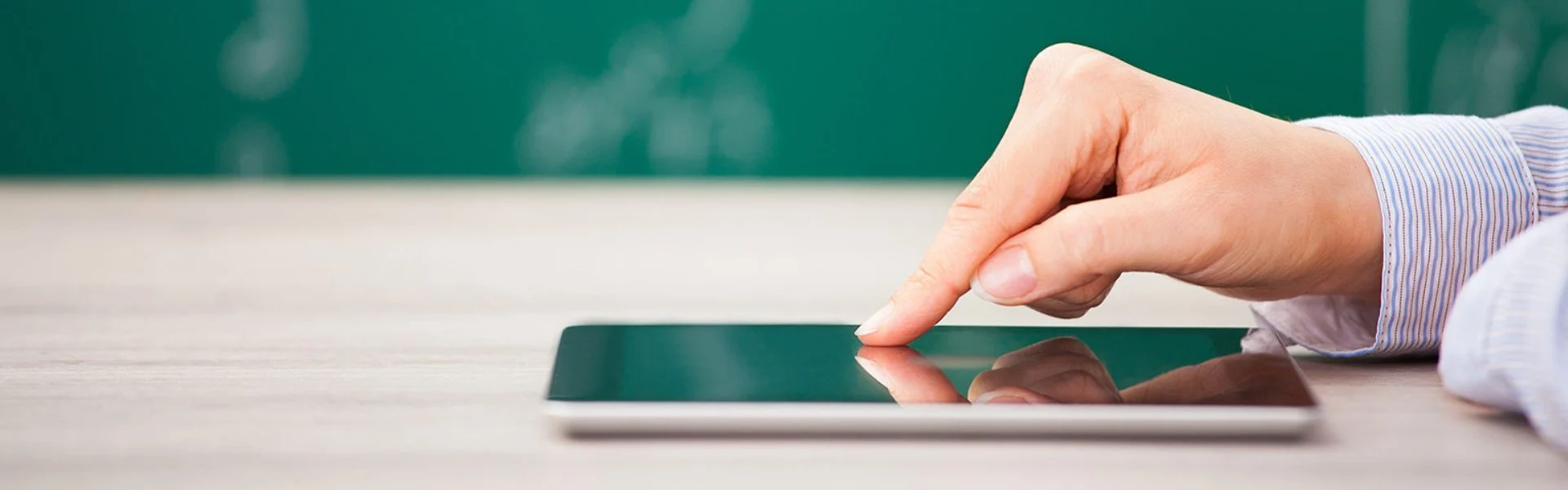 Vor einer Tafel liegt ein Handy auf einem Tisch. Eine Hand wischt über den Bildschirm. Link zum Projekt
