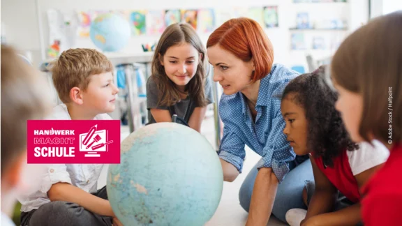 Lehrerin betrachtet mit drei Schüler:innen einen Globus